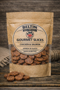 A stand-up kraft paper pouch of Beltin Pet Treats Gourmet Slices Chicken & Salmon, with several slices spilled in front on a rustic wooden surface.
