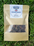A kraft paper pouch of Bellin Chicken Hearts appetizers, placed on a green grass background. The pouch has a clear window showing the dark, textured appetizers inside, and a white circular label with the Bellin brand logo.